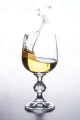White wine splashing in wine glass on light background. .