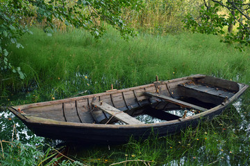 Old weathered wooden rowing boat with water left to overgrown lake.