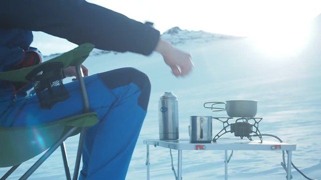 Camping in winter mountains. Climber mountaineer csitting in chair ooking outdoor in winter. Tourist backpacker travelling in winter, high snow mountains , trekking and camping equipment, camping tent
