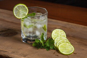 Summer cocktail mojito in glass, sliced lime and mint on wooden background..