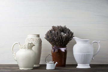 Flowers in neutral colored vases, candles on rustic wooden shelf against shabby white wall. Home decor.