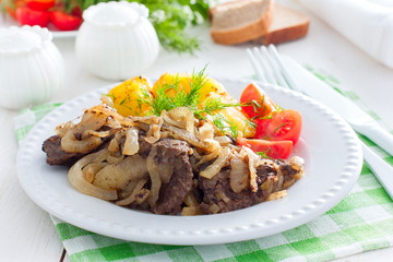 Fried beef liver with onions on a white plate with potatoes and fresh tomatoes, horizontal