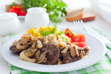 Fried beef liver with onions on a white plate with potatoes and fresh tomatoes, horizontal
