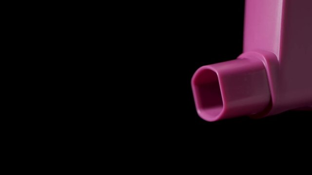 Pink asthma inhaler with spray coming out on black background. Slow motion 25%.