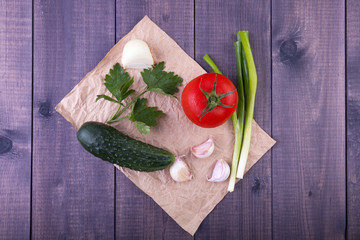 Cucumber, garlic, onion, parsley and tomato vegetables still life. rumpled paper background on wood. Top view