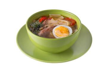Chicken soup with noodels, meat pieces, herbs and egg in bowl on white background