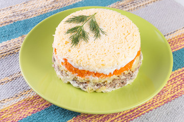 Layered fish salad with vegetables and salmon Mimosa on a plate on tablecloth