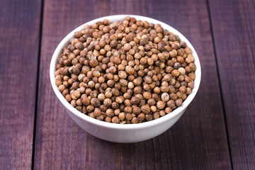 Coriander seeds in a white bowl on a wooden background. Angle view