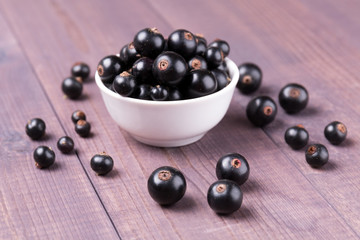 Ripe blackcurrant in a bowl isolated on a wooden background. Angle view