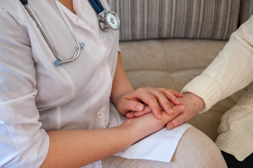 Pretty nurse in white coat helps sick retiree on social assistance program. Nurse carefully examines prescription of drugs, makes injections, measures blood pressure and cares.