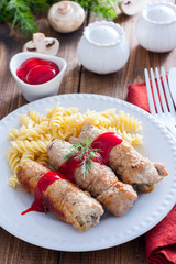Small pork rolls with champignons on a white plate with pasta and ketchup, selective focus