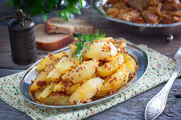 Sliced roasted mustard potatoes with grains on a metal platter, horizontal
