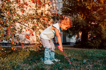 Little toddler girl playing with soap bubbles in summer park. Happy kid having fun outdoors