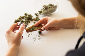 Woman rolling a marijuana blunt on white background. Cannabis use concept. Woman preparing and...