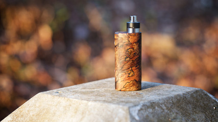high end natural stabilized wood box mods with rebuildable dripping atomizer on bokeh texture background, vaping device, selective focus