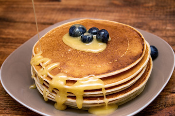 Pancakes with blueberries and honey on the dark brown wooden background