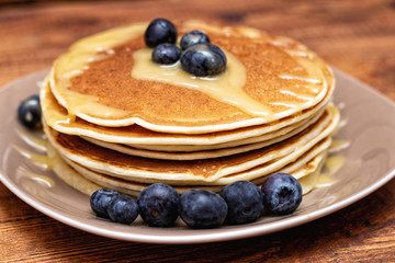 Pancakes with blueberries and honey on the dark brown wooden background