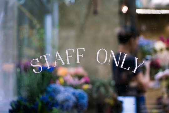 Staff only sign on window with blurry background of florist working in floral shop