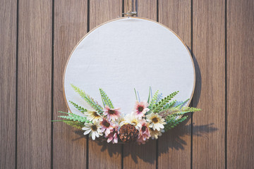 Wooden embroidery hoop with white plain fabric and flower decoration hanging on wooden pattern wall © tarapatta