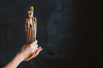 Painter tools set. Work and lifestyle. Assorted brushes bunch in woman hands. Copy space on black background.