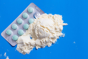 Protein powder in measuring plastic spoon and vitamin complex, omega 3, glucosamine capsules, supplements on blue background, sports nutrition, top view.