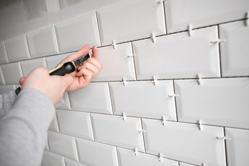 Ceramic tile lying. Installing new subway or metro tiles in bathroom, shower or kitchen back splash during home renovation. Placing or taking out tile spacers with hands and pliers.