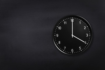 Black wall clock showing four o'clock on black chalkboard background. Office clock showing 4am or 4pm on black texture