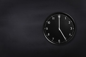 Black wall clock showing five o'clock on black chalkboard background. Office clock showing 5am or...