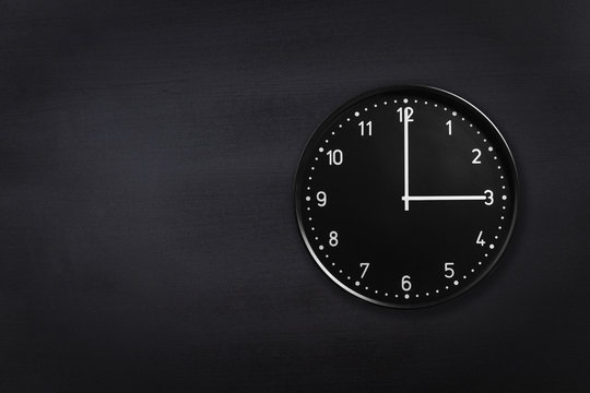 Black wall clock showing three o'clock on black chalkboard background. Office clock showing 3am or 3pm on black texture