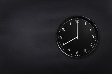 Black wall clock showing eight o'clock on black chalkboard background. Office clock showing 8am or 8pm on black texture