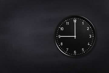 Black wall clock showing nine o'clock on black chalkboard background. Office clock showing 9am or...
