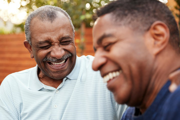 Senior black man and his adult son laughing together outdoors, close up