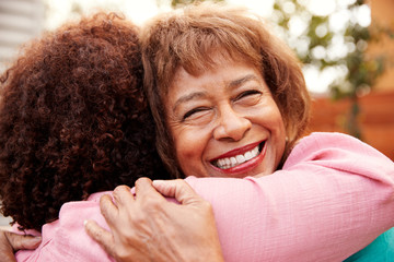 Senior black mum and her middle aged daughter embracing outdoors, close up