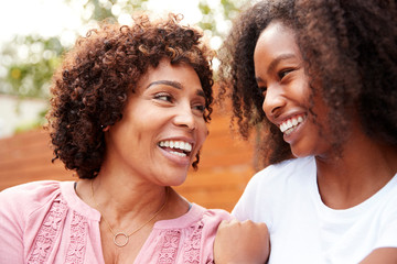 Middle aged black mum and teen daughter smiling at each other
