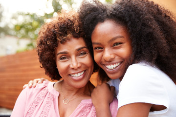 Middle aged black mum and teenage daughter embracing and smiling to camera - Powered by Adobe