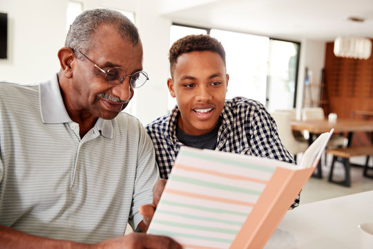 Young black man looking at a photo album at home with his grandfather, close up