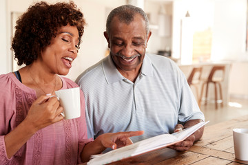 Senior black man and his middle aged daughter looking through photo album together at home, close up