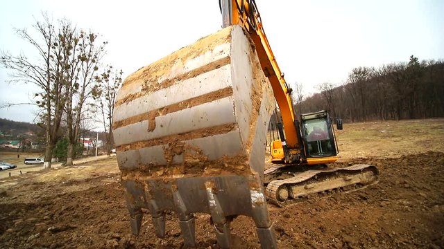 Close-up of a excavator bucket that throws out the earth. Slow motion of a digger digging a pit and throwing dirt. Shot by wide angle lens