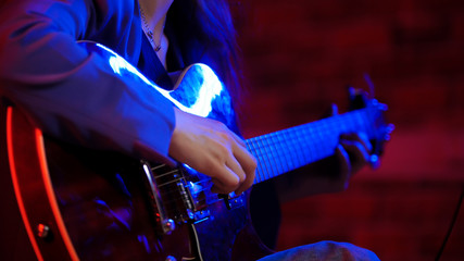 A young woman playing guitar in neon lighting