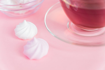 Obraz na płótnie Canvas White and pink twisted meringues and cup of tea on pink background. French dessert prepared from whipped with sugar and baked egg whites. Greeting card with copy space