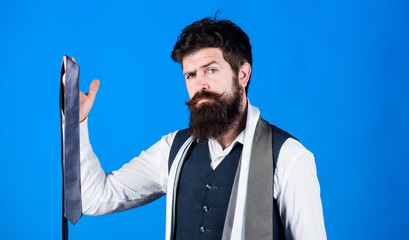 Match colors. Man bearded hipster hold few neckties on blue background. Guy with beard choosing...