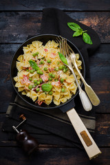 Fettuccine pasta with bacon and green peas and parmesan cheese in old pan on old dark wooden background. Top view.