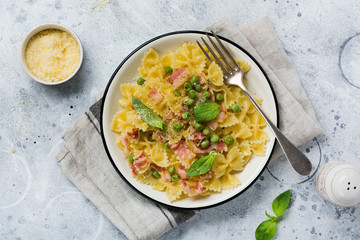 Fettuccine pasta with bacon and green peas and parmesan cheese in light plate on old gray concrete background. Top view.