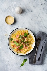 Fettuccine pasta with bacon and green peas and parmesan cheese in light plate on old gray concrete background. Top view.