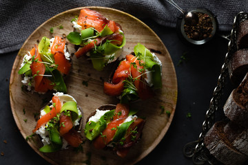 Top view of homemade toast sandwich with salmon, avocado, cottage cheese and microgreen sprouts on dark board background. View from above of healthy food - breakfast