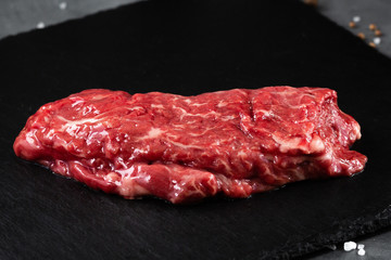 Raw meat, beef butcher or machete steak on black Slate board with Grill pan, knife with spices on a gray table