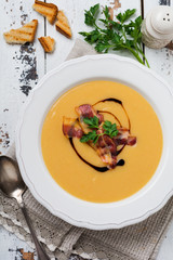 Potato soup cream with bacon and soy sauce in white bowl, on light old wooden background. Top view.