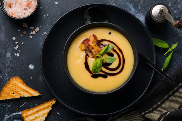 Potato soup cream with bacon and soy sauce in black bowl, on dark old concrete background. Top view.