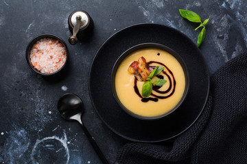 Potato soup cream with bacon and soy sauce in black bowl, on dark old concrete background. Top view.