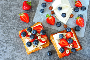 Healthy toasts with white cheese, fresh strawberries and blueberries. The concept of a healthy snack or lunch. 